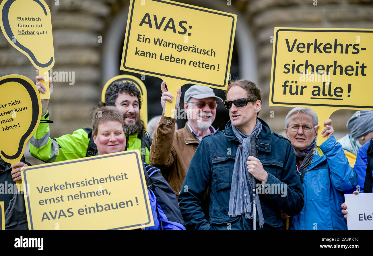 Hamburg, Germany. 09th Oct, 2019. Members of the Association for the Blind and Visually Impaired hold in their hands signs with the inscriptions 'Wir sind ganz Ohr für E-Fahrzeuge', 'AVAS: Ein Warngeräusch kann Leben sparen!', 'Verkehrssicherheit für alle!' and 'Verkehrssicherheit ernst nehmen, AVAS einbauen!' during a protest action on the town hall market. The action is directed against public funds for e-vehicles without warning noise. Credit: Axel Heimken/dpa/Alamy Live News Stock Photo