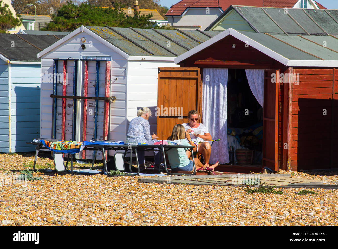 19 September 2019 Owners enjoying the sun at theit traditional family beach hut on the pebble beach at Hayling Island in Hampshire on the south coast Stock Photo
