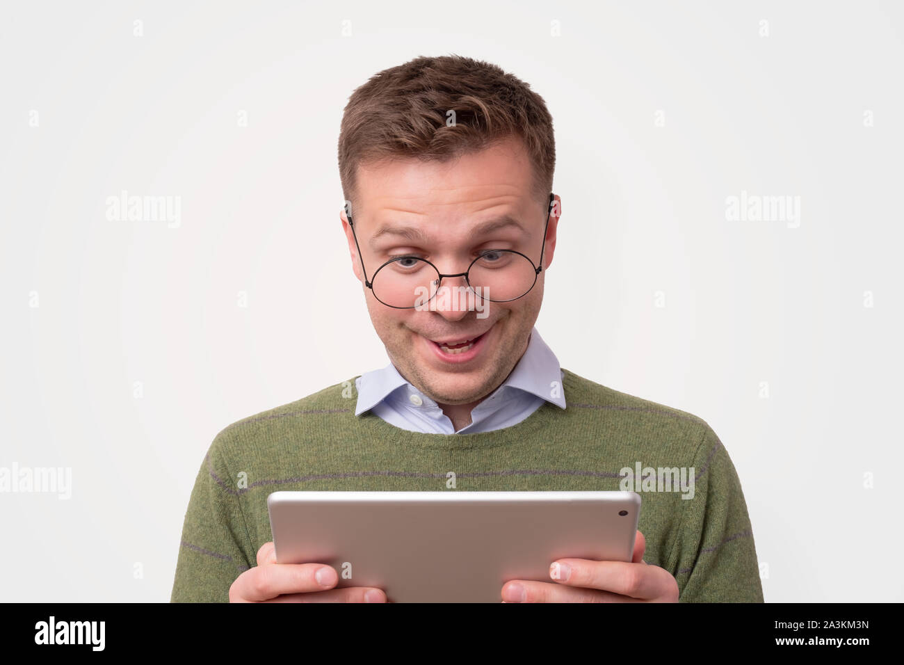 Handsome surprised young man wearing green sweater looking on tablet Stock Photo