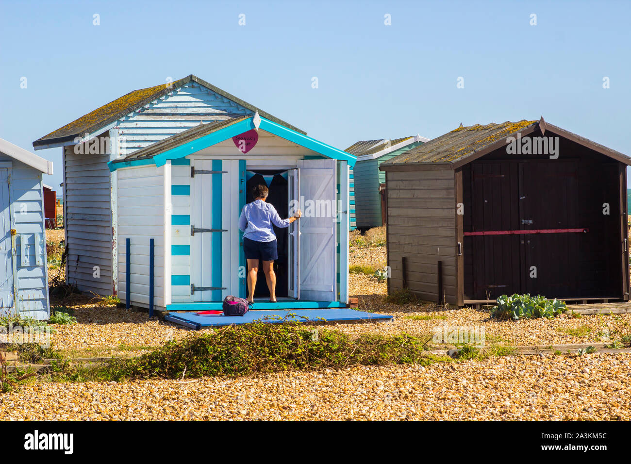 19 September 2019 A woman owner opening up her traditional family beach huts flanked my wild beach plants at Hayling Island beach on the south Stock Photo
