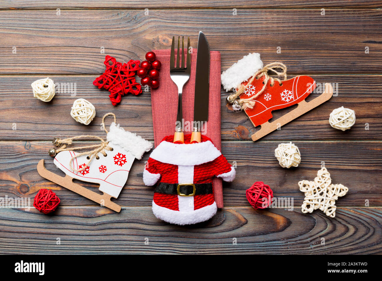 Top view of fork and knife on napkin on wooden background. Different christmas decorations and toys. Close up of New Year dinner concept. Stock Photo