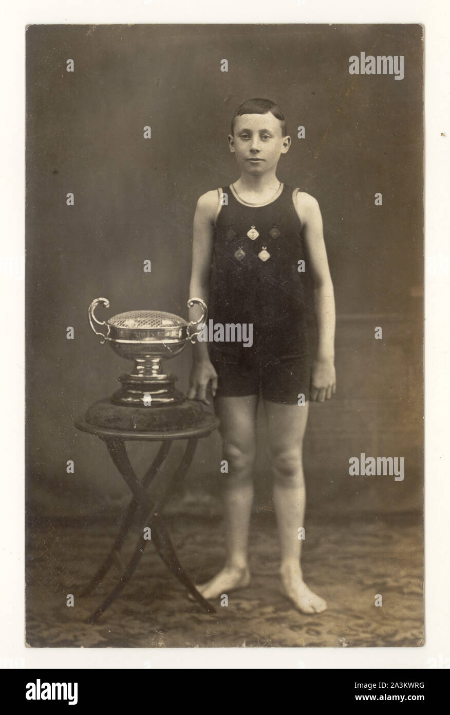Early 1900's postcard of slim young boy wearing P.E. or swimming kit, with medals on his swimming costume, standing next to trophy cup, Hamilton, Lanarkshire, Scotland, U.K. Stock Photo