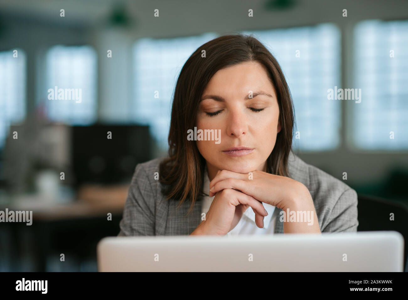 Tired businsswoman sitting with her eyes closed at her desk Stock Photo