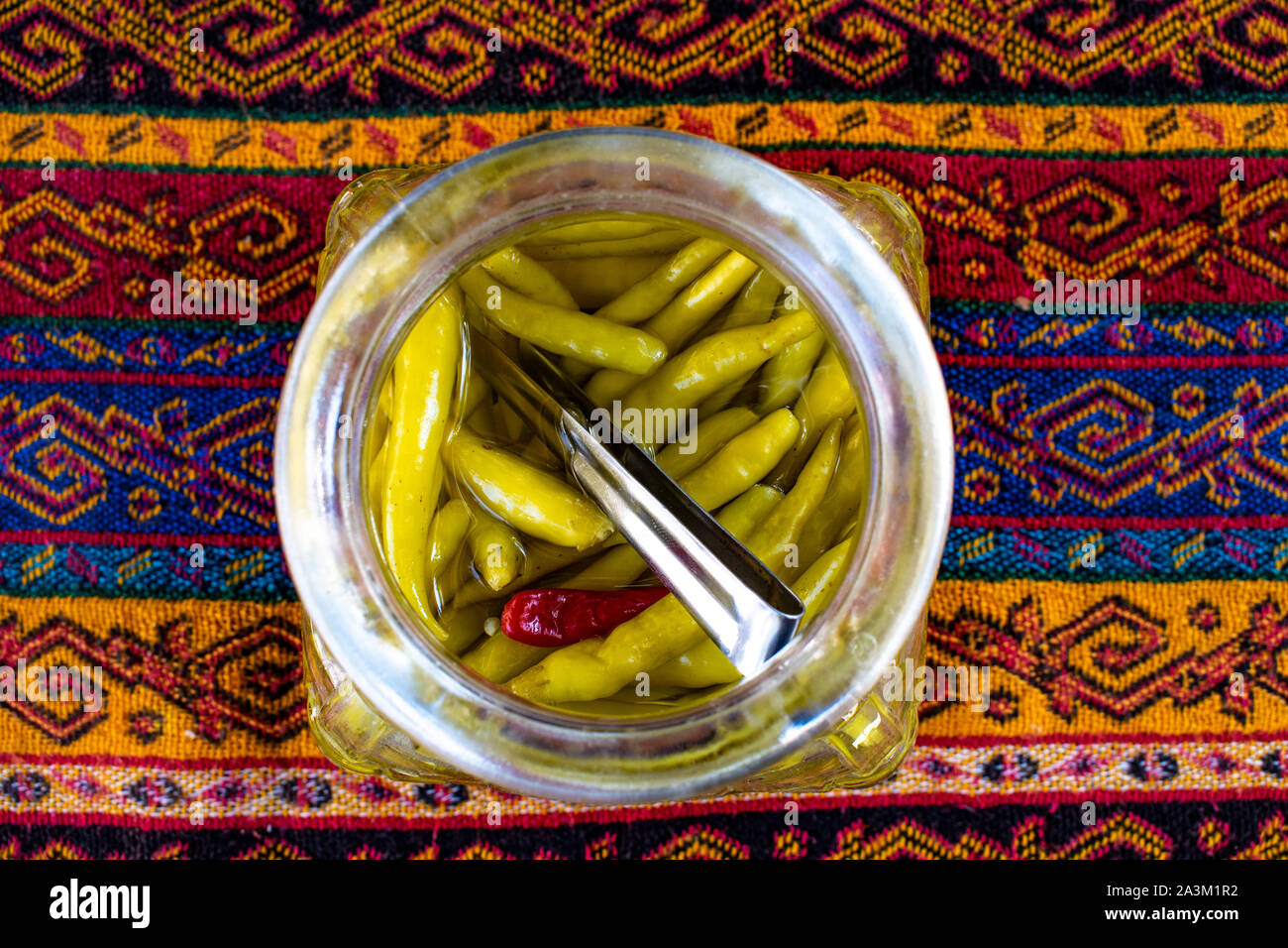 Istanbul, Turkey: Middle Eastern food and lifestyle, a jar of spicy green chillies and hot pepper on a damask tablecloth Stock Photo