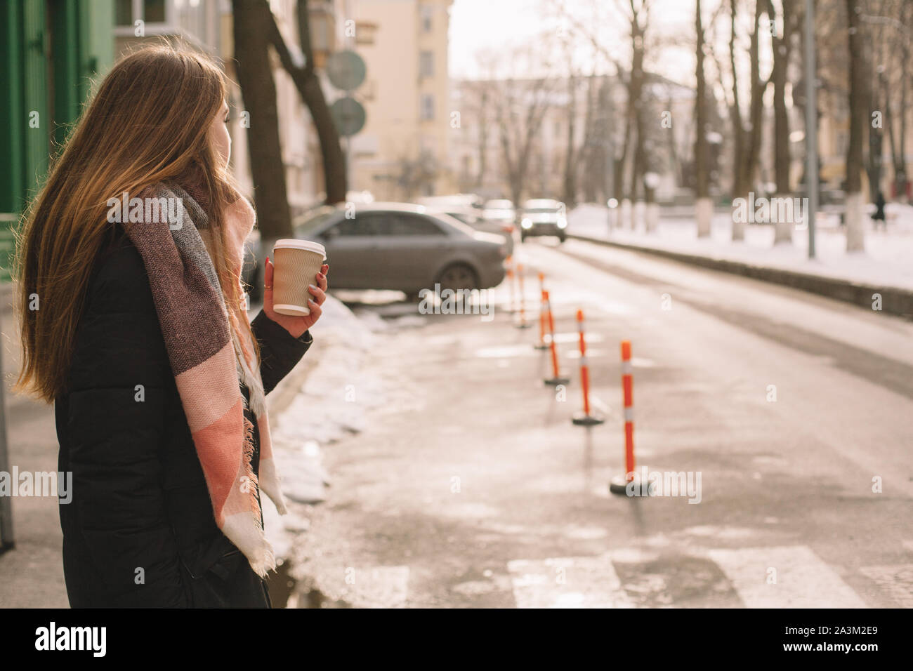 Woman with disposable cup in warm clothing crossing city street in winter Stock Photo