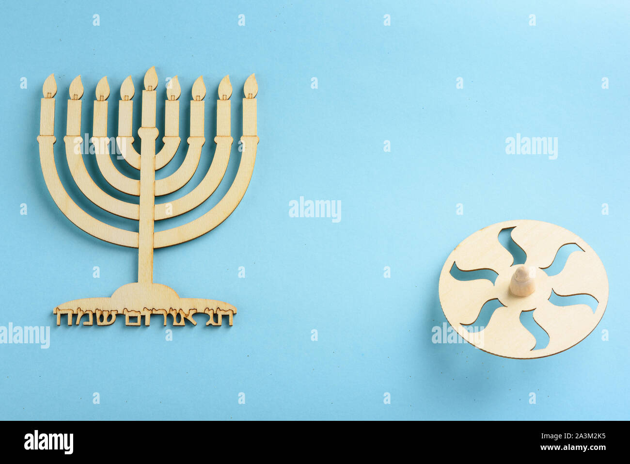 Children's craft -Wood menorah and wooden dreidels spinning top symbols Jewish holiday Hanukkah on blue background. Written in Hebrew happy Hanukah. Stock Photo