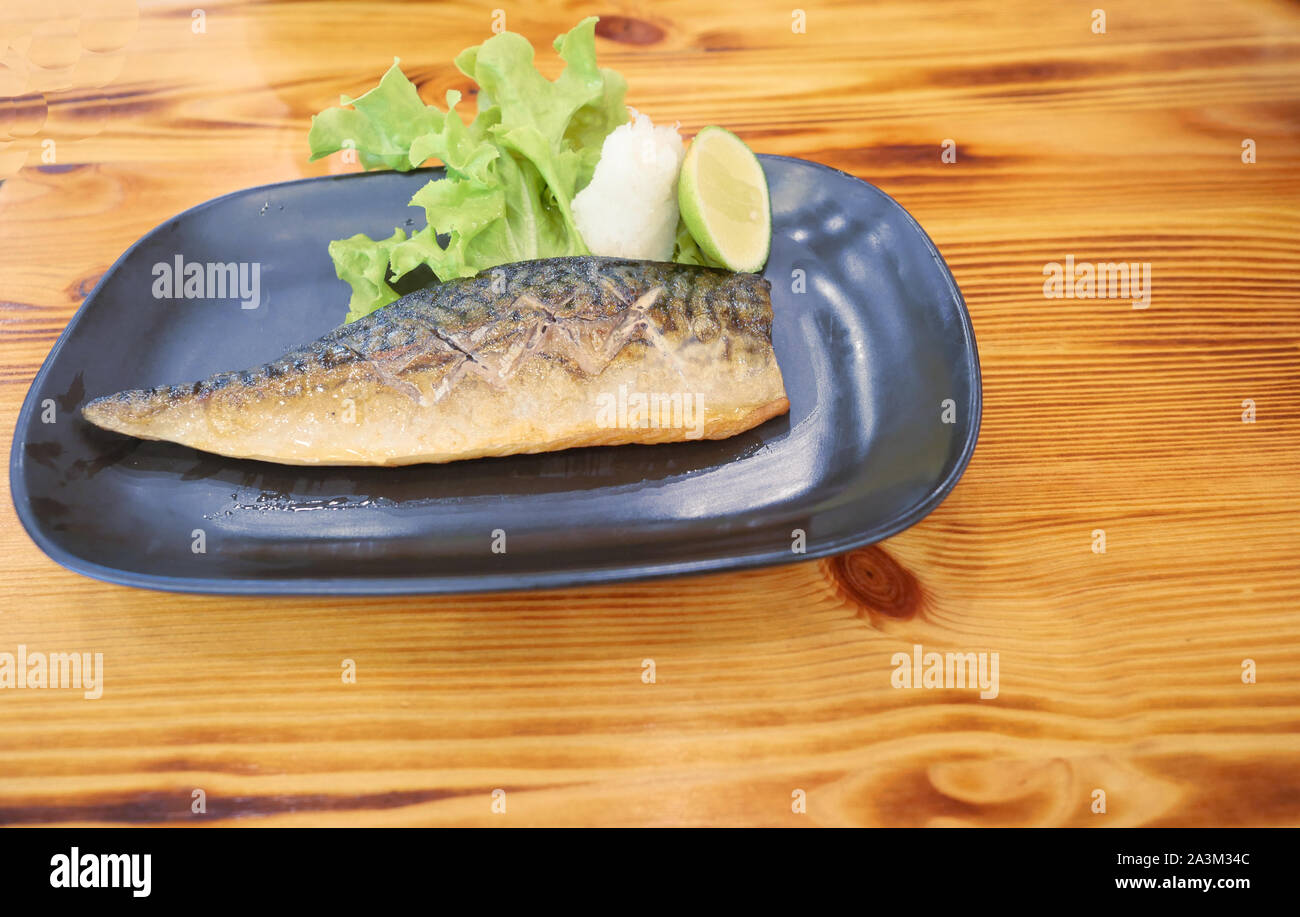 Grilled Saba or Mackerel fish with Sliced Lime fruit and Shredded radish, Japanese seafood with green salad on a black plate, Asian food with brown wo Stock Photo