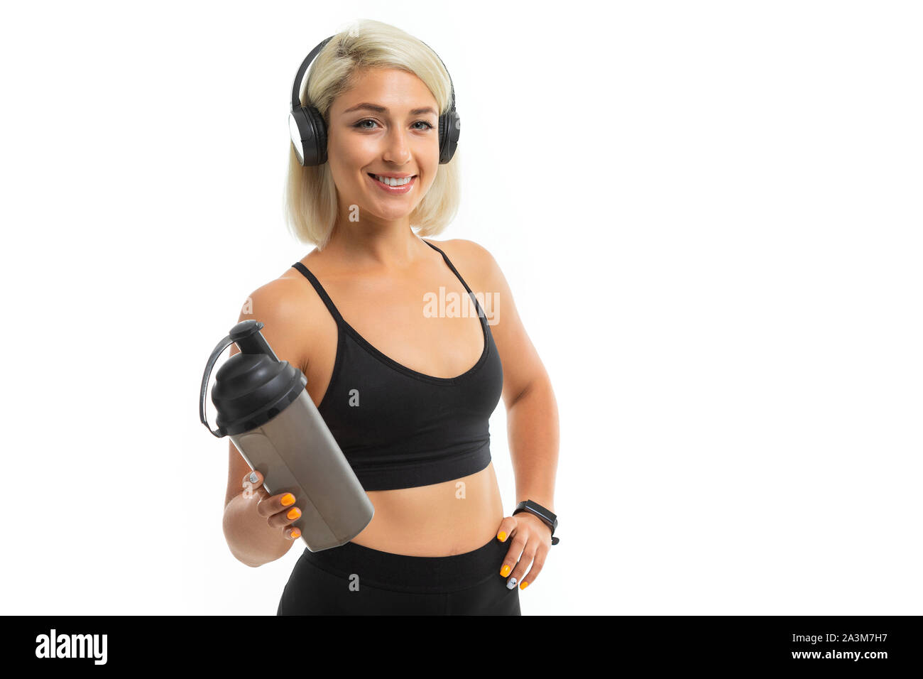 A sports girl with blonde hair and bright manicure in headphones black sports topics and leggings holds a sports water bottle Stock Photo Alamy