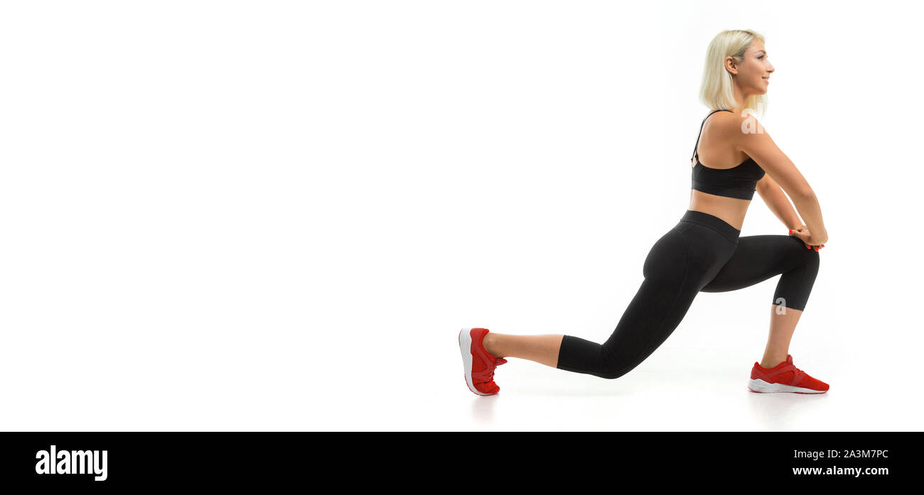 A young sports girl with blonde hair and bright manicure in black sports topics, leggings and sneakers does exercises. Stock Photo