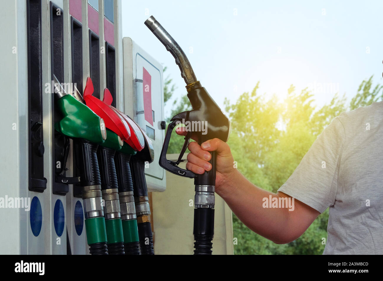 Man fills up his car with a gasoline at gas station. Petrol station pump. To fill car with fuel. Gasoline and oil products concept. Sunlight. Stock Photo