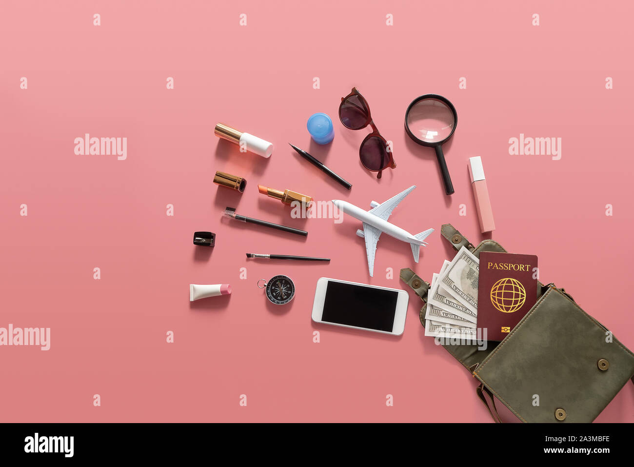 Flat lay of green leather woman shoulder bag open out with cosmetics, accessories , smartphone , money and passport on pink background Stock Photo