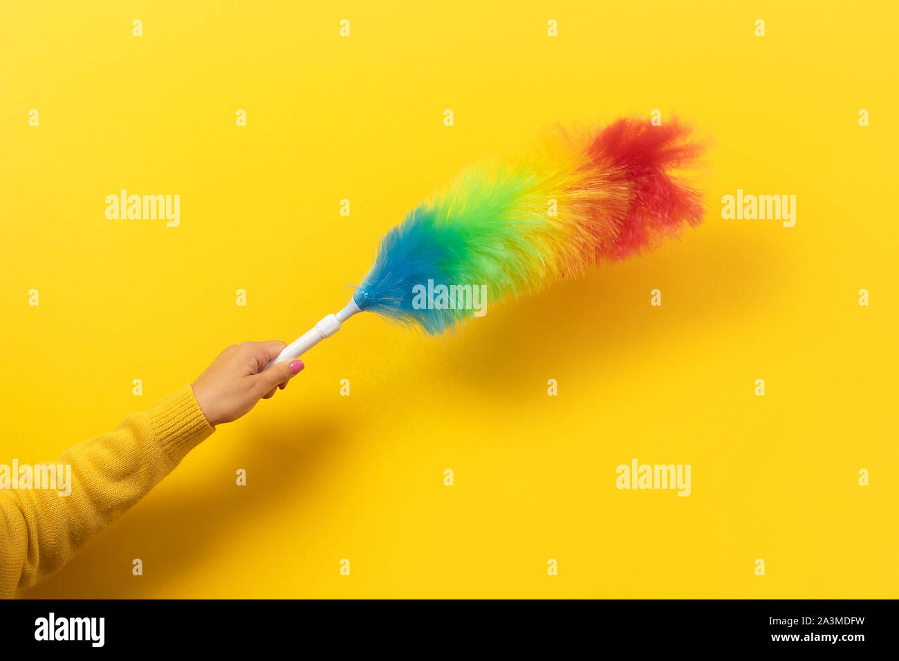 Colorful feather duster in hand on yellow background. Cleaning concept. Stock Photo