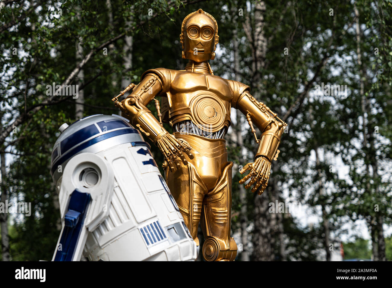 Izhevsk Russia 07.09.2018 Statues of robots from Star Wars movie, r2d2 and c3p0 outdoors, golden and white robots with trees on background Stock Photo