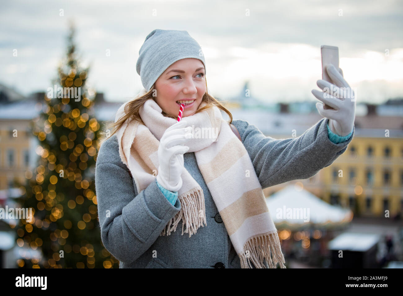 Young woman in Christmas market eating candy cane and taking selfie. Girl  in knitted warm hat and scarf. Illuminated and decorated fair kiosks, shops  Stock Photo - Alamy