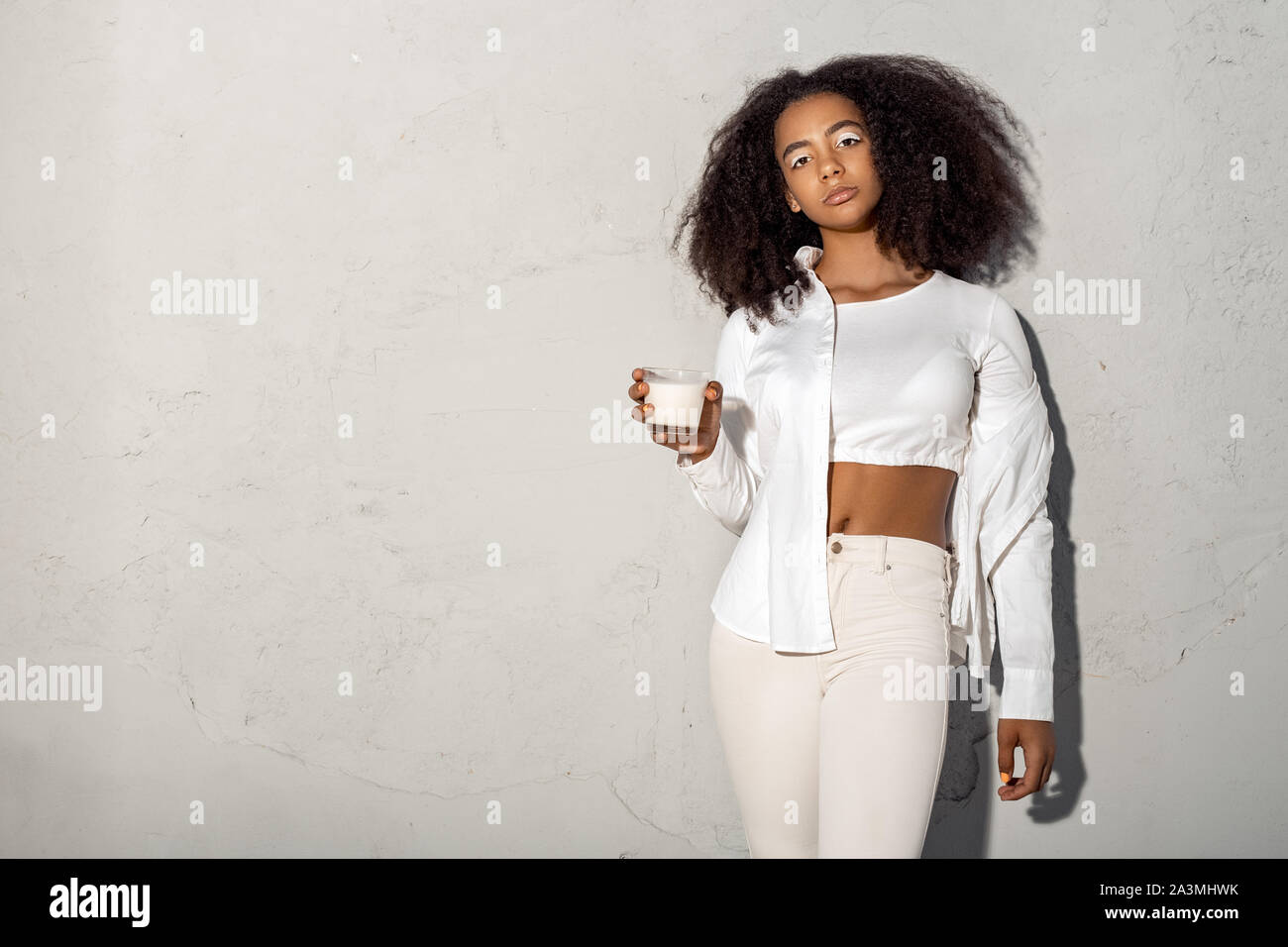 Freestyle. African girl in white outfit with bare belly standing isolated  on gray posing with glass of milk cool copy space Stock Photo - Alamy