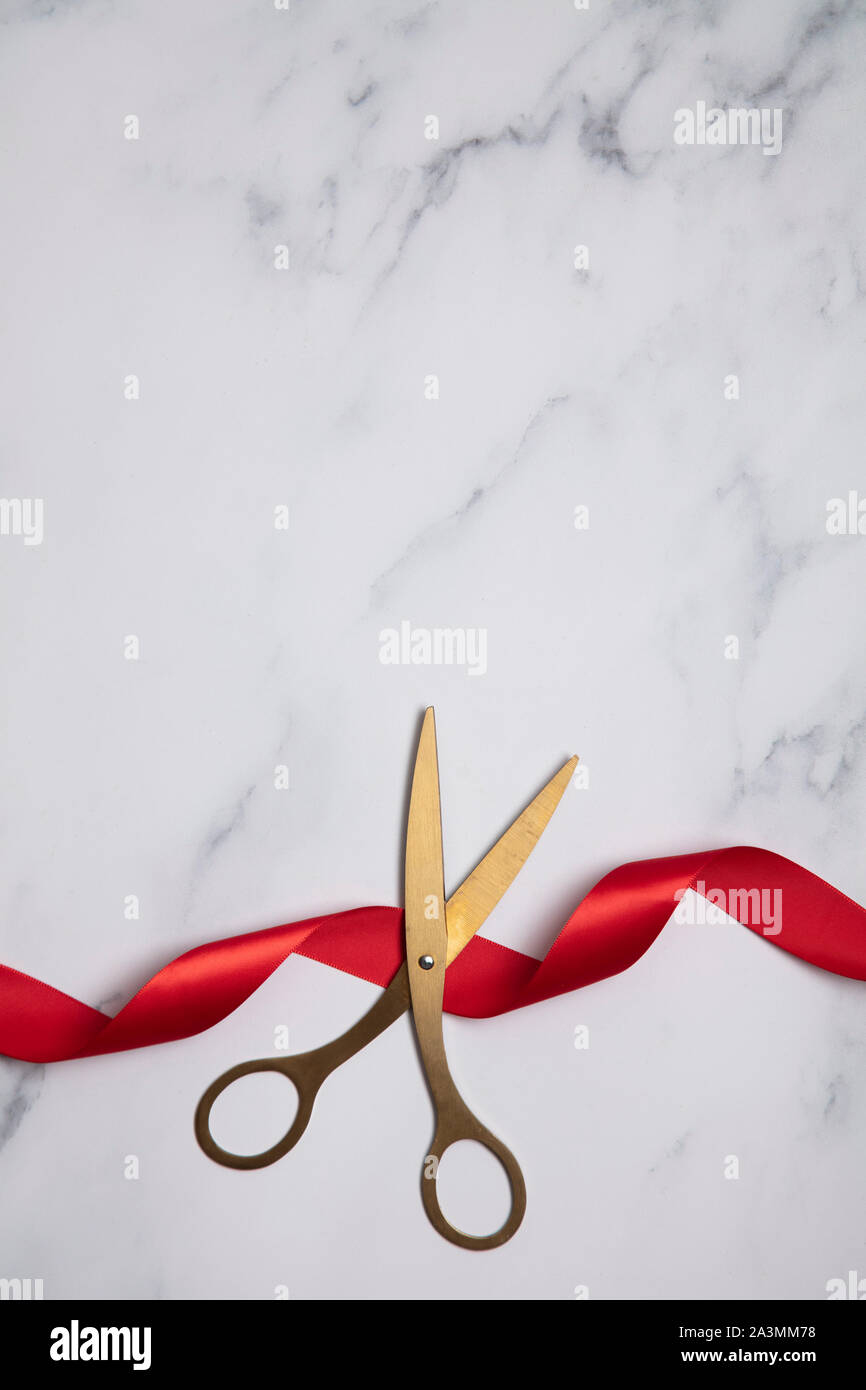 Grand opening background. Gold scissors with red ribbon on a marble