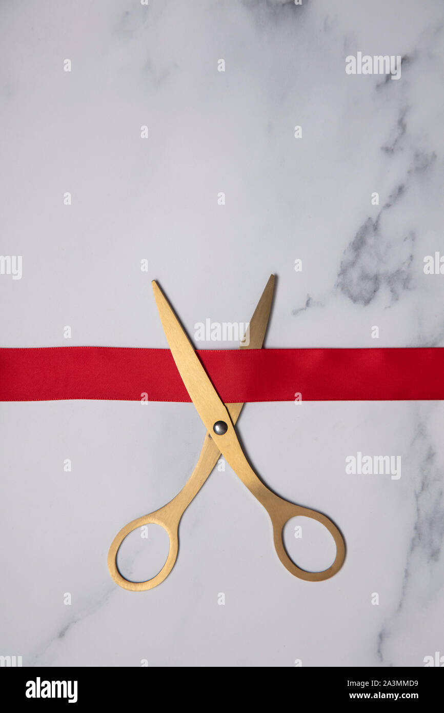 Grand opening background. Gold scissors with red ribbon on a marble