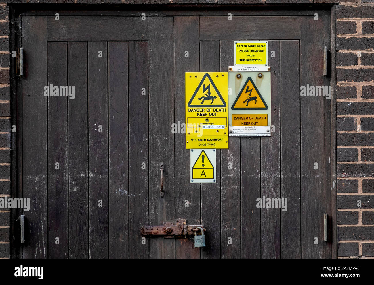 Workplace safety: caution Danger of Death triangular warning signs on town centre substation; Copper earth cable has been removed from this electricty substation, Southport, UK Stock Photo