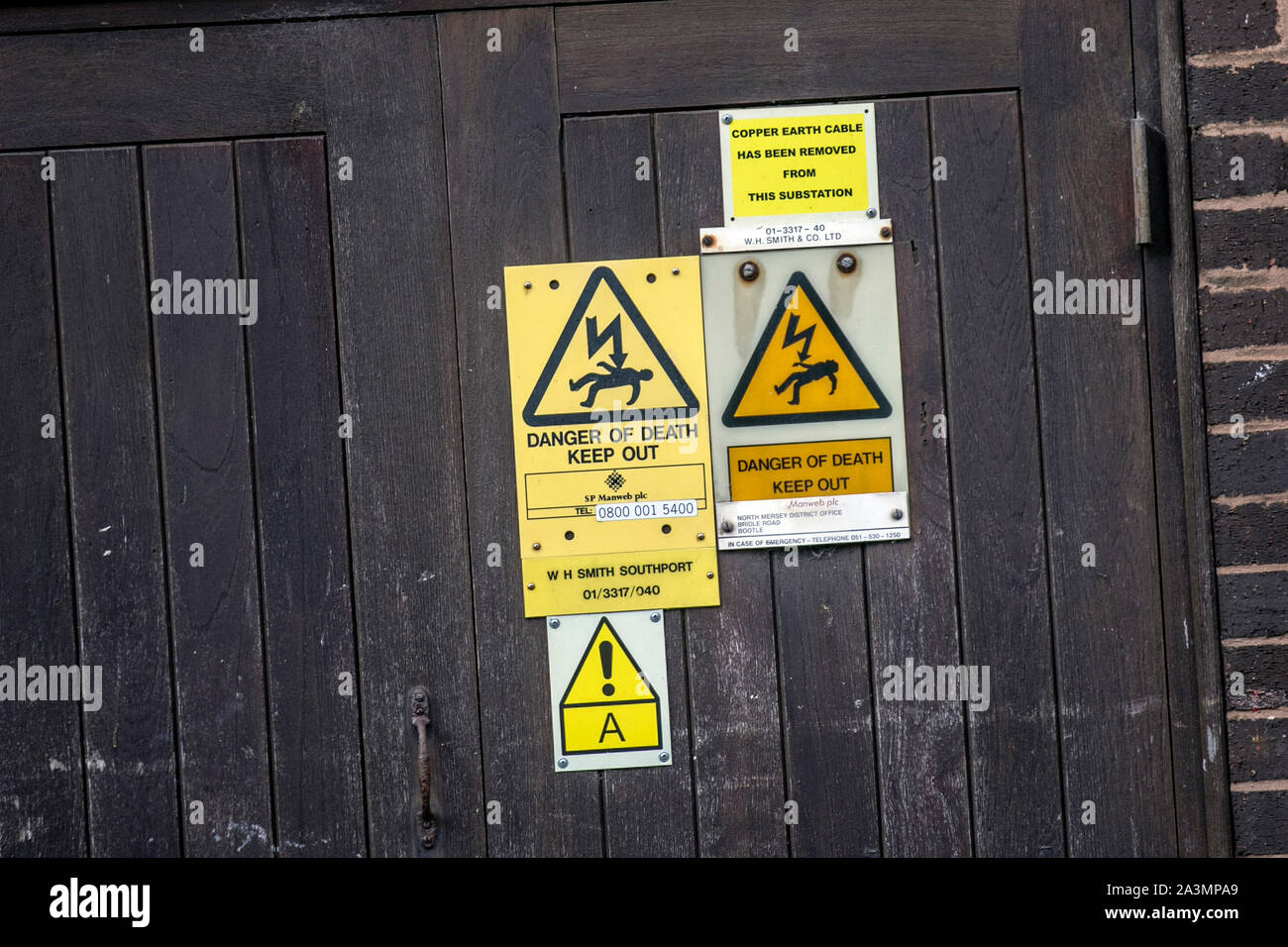 Workplace safety: caution Danger of Death triangular yellow warning signs on town centre substation; Copper earth cable has been removed from this electricity substation, Southport, UK Stock Photo