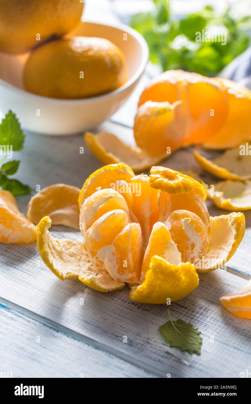 Tangerines with peel and mellisa herbs on table. Ripe fresh tropical fruit on wooden board Stock Photo