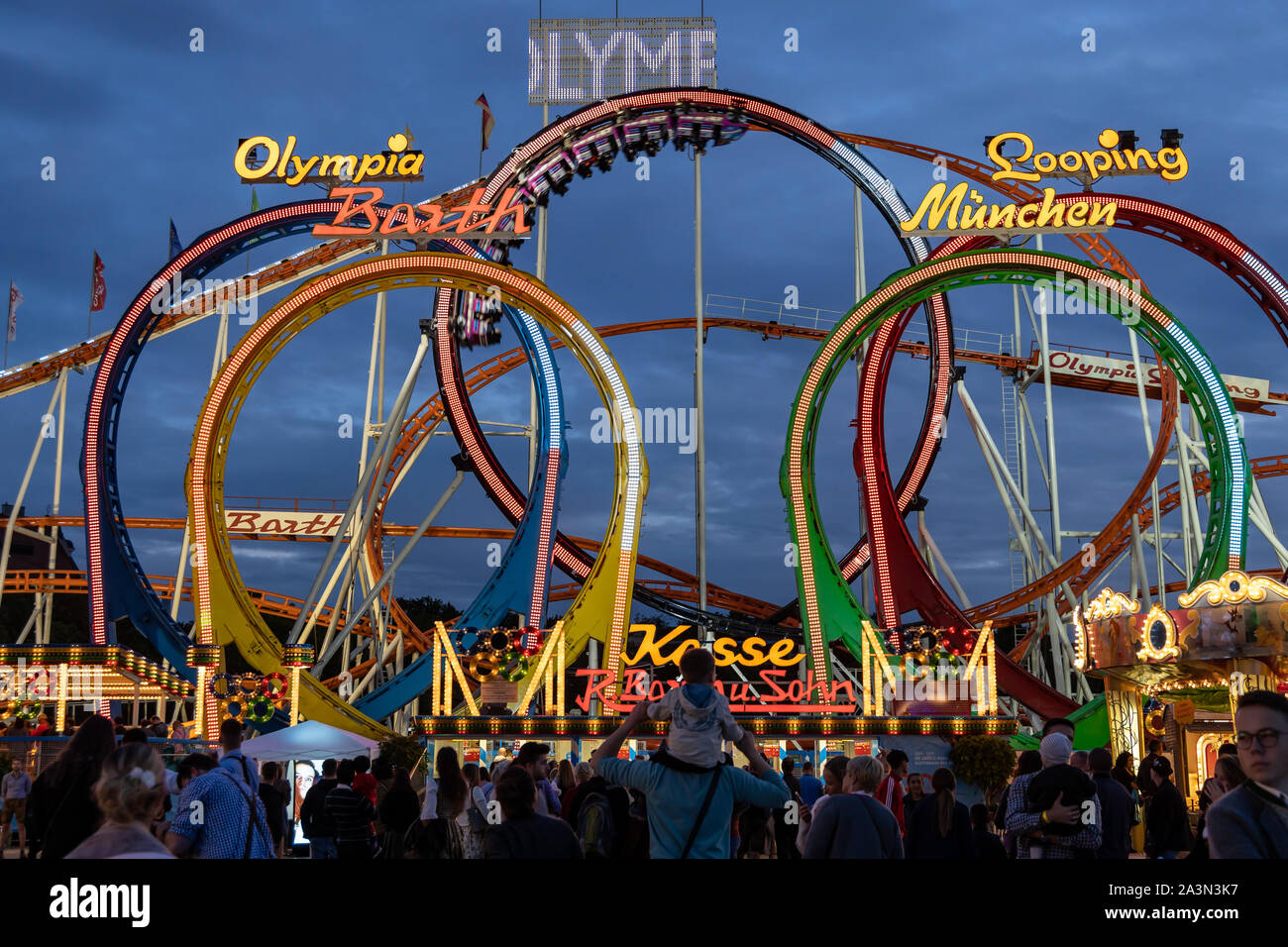 Munich, Germany - September 24: a father is carrying his young son on his shoulders in front of a 5 loop roller coaster on the oktoberfest. Stock Photo