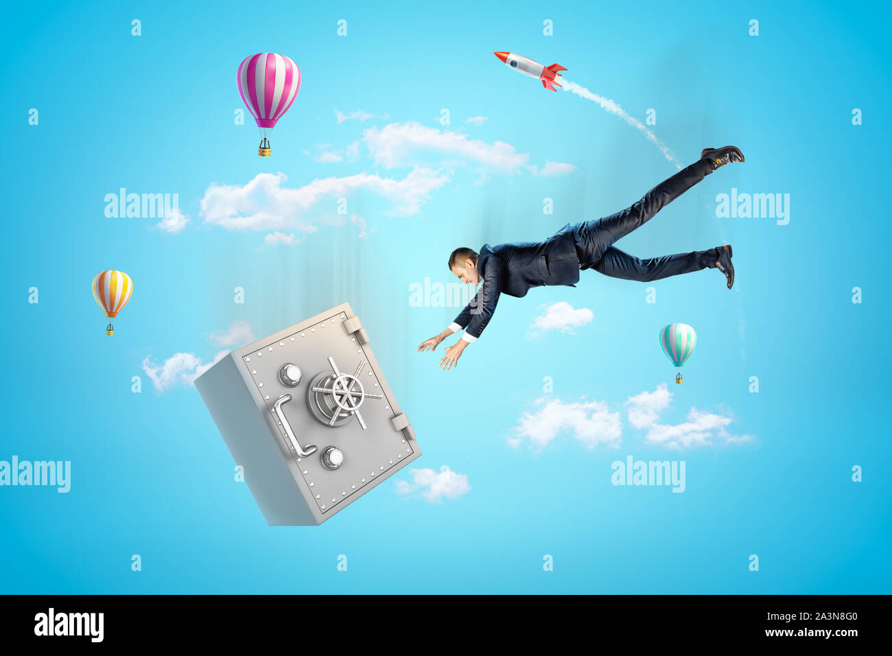 Young businessman falling down in blue sky trying to catch big metal safe, with hot air balloons and rocket in background. Stock Photo