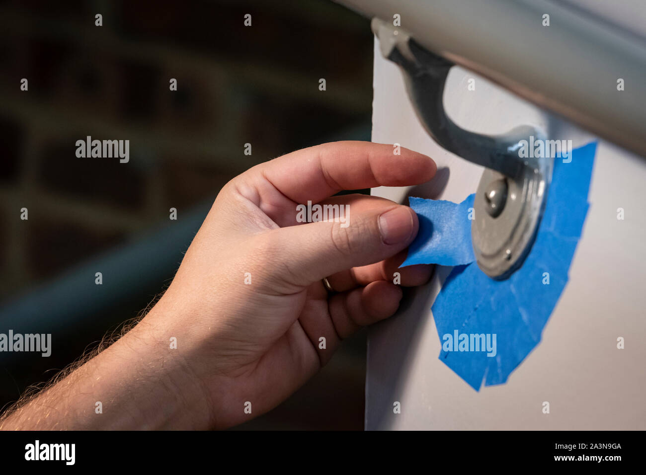 Hand taping off edge of hand rail with blue painter's tape to prep for fresh coat of paint Stock