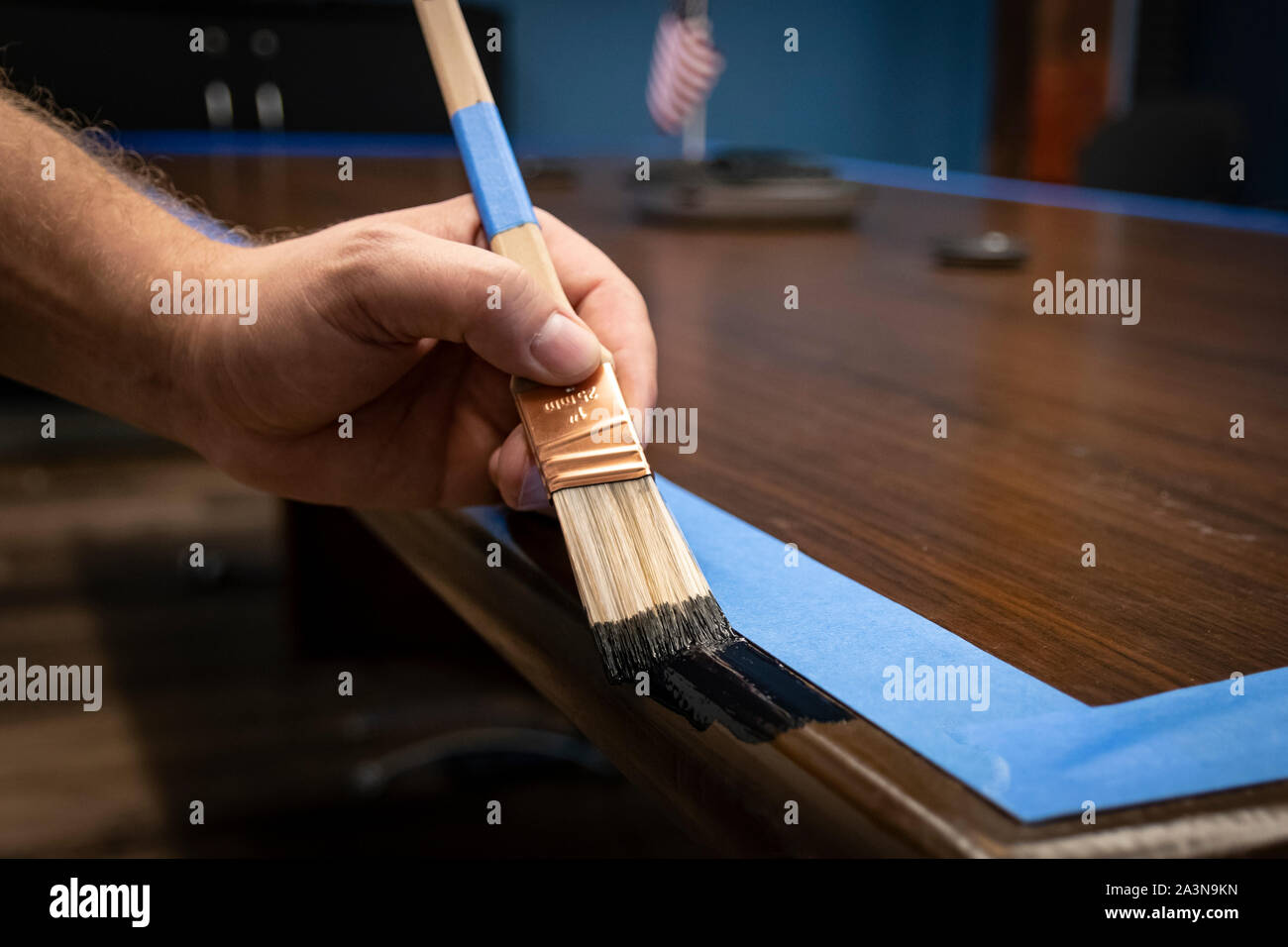 Hand painting conference table edge/trim; prepped with blue painter's tape Stock Photo