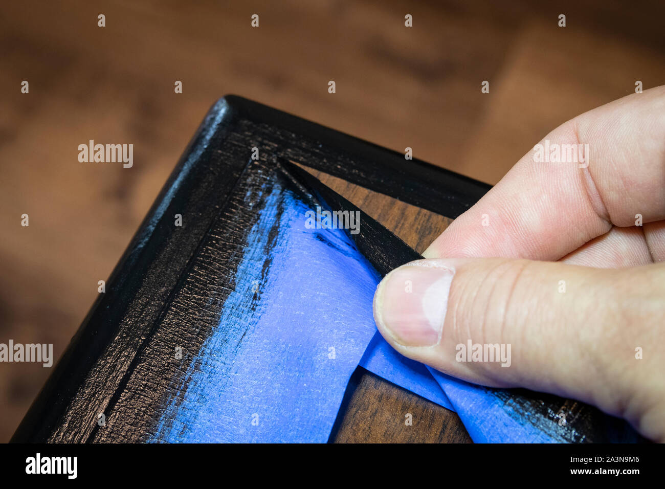 Hand removing blue painter's tape from edge of refinished furniture paint job Stock Photo Alamy
