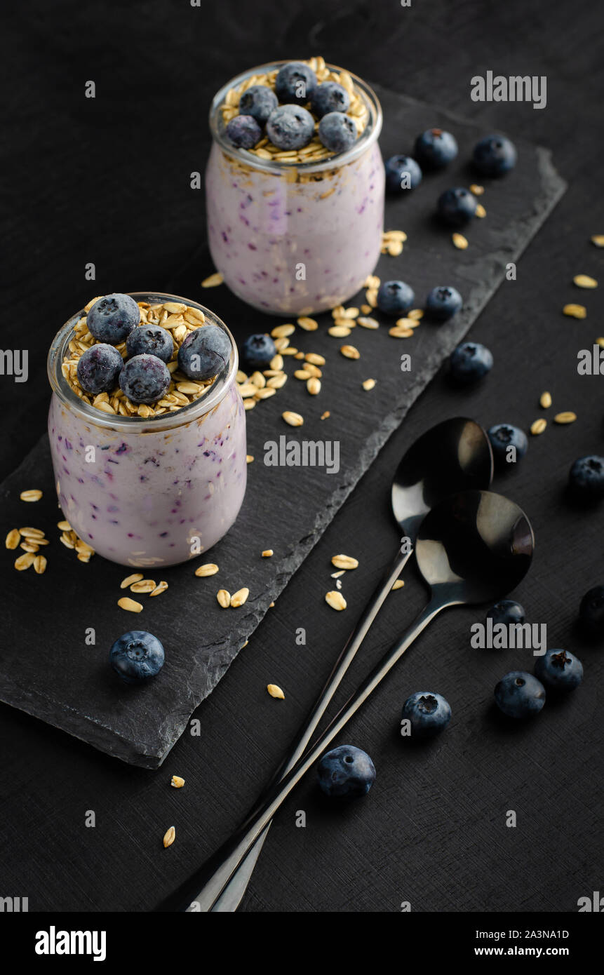 Healthy breakfast concept. Jars of homemade yogurt with blueberries and oats on black background. Vertical. Stock Photo