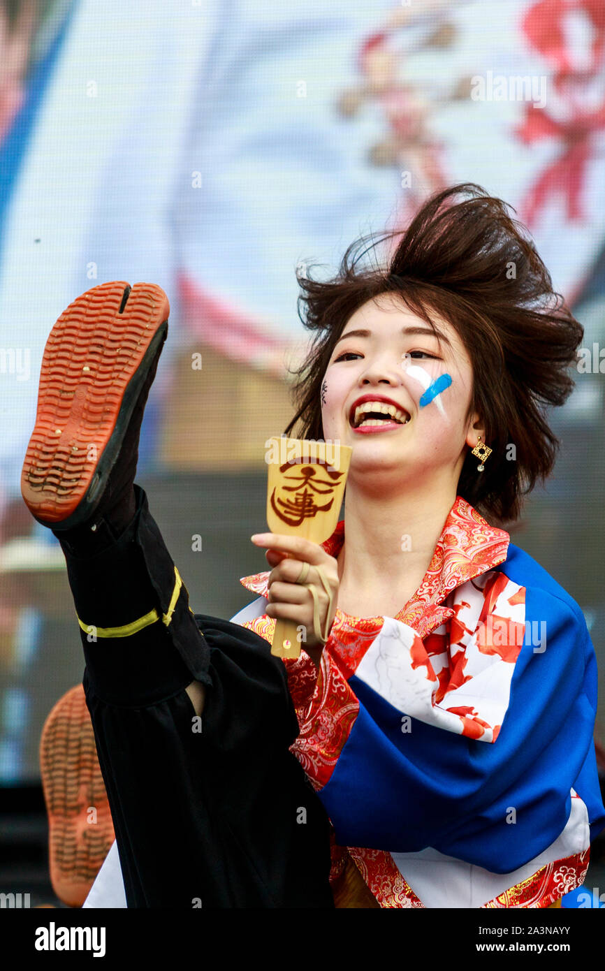 Hinokuni Yosakoi festival in Japan. Close up of smiling young woman dancer holding naruko, clapper, and kicking her leg up high, wears Jika-tabi shoe. Stock Photo