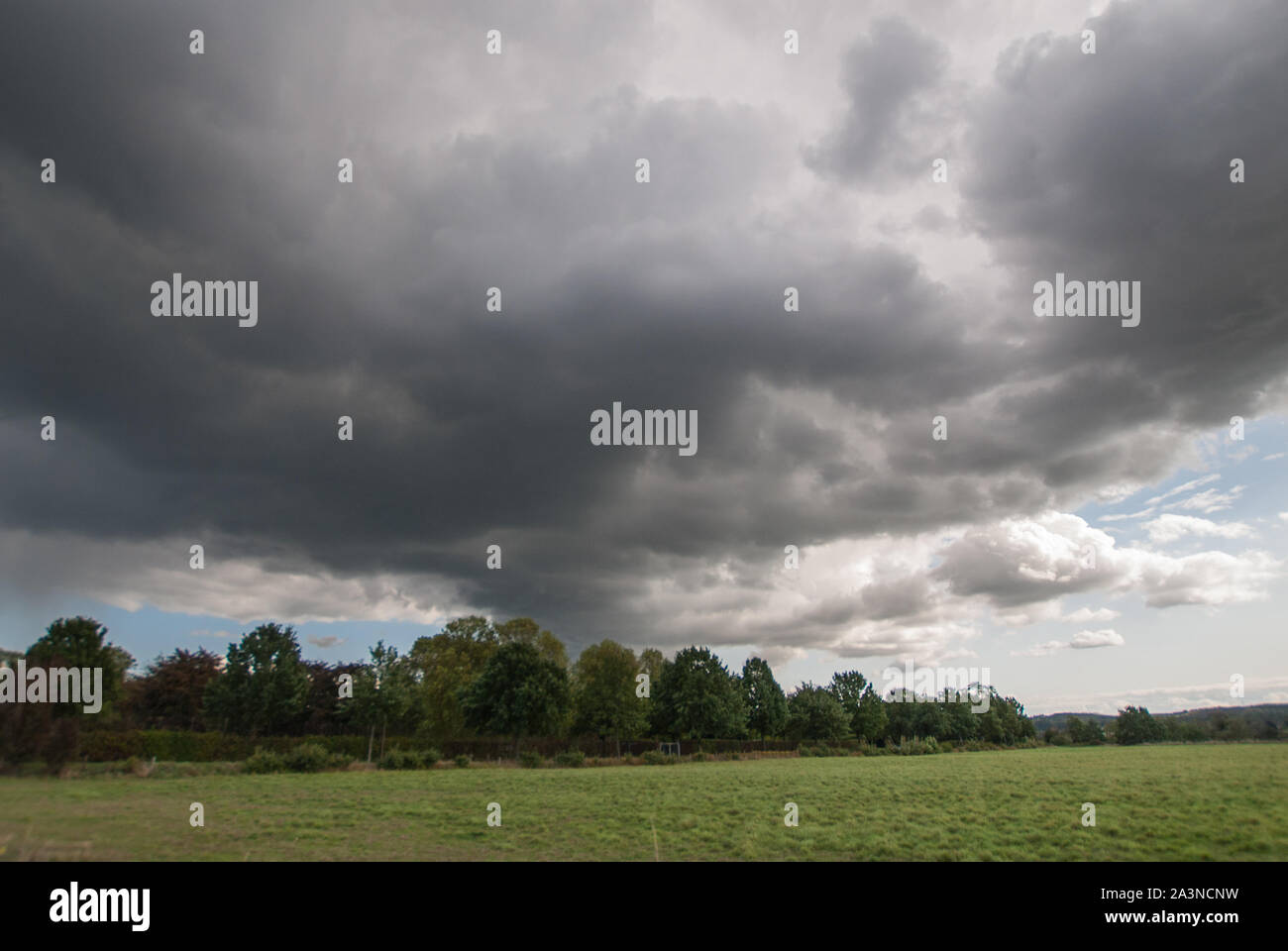 Dramatic dark rain clouds over a grove on the field edge. Stock Photo