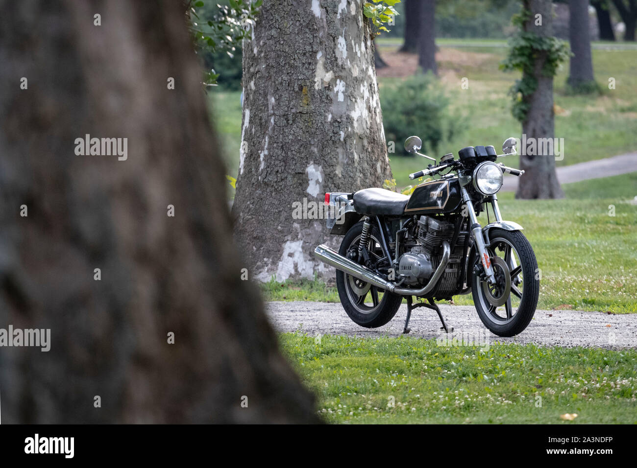 Black vintage Yamaha XS500 motorcycle stands alone against in nature and wooded trail area Stock Photo