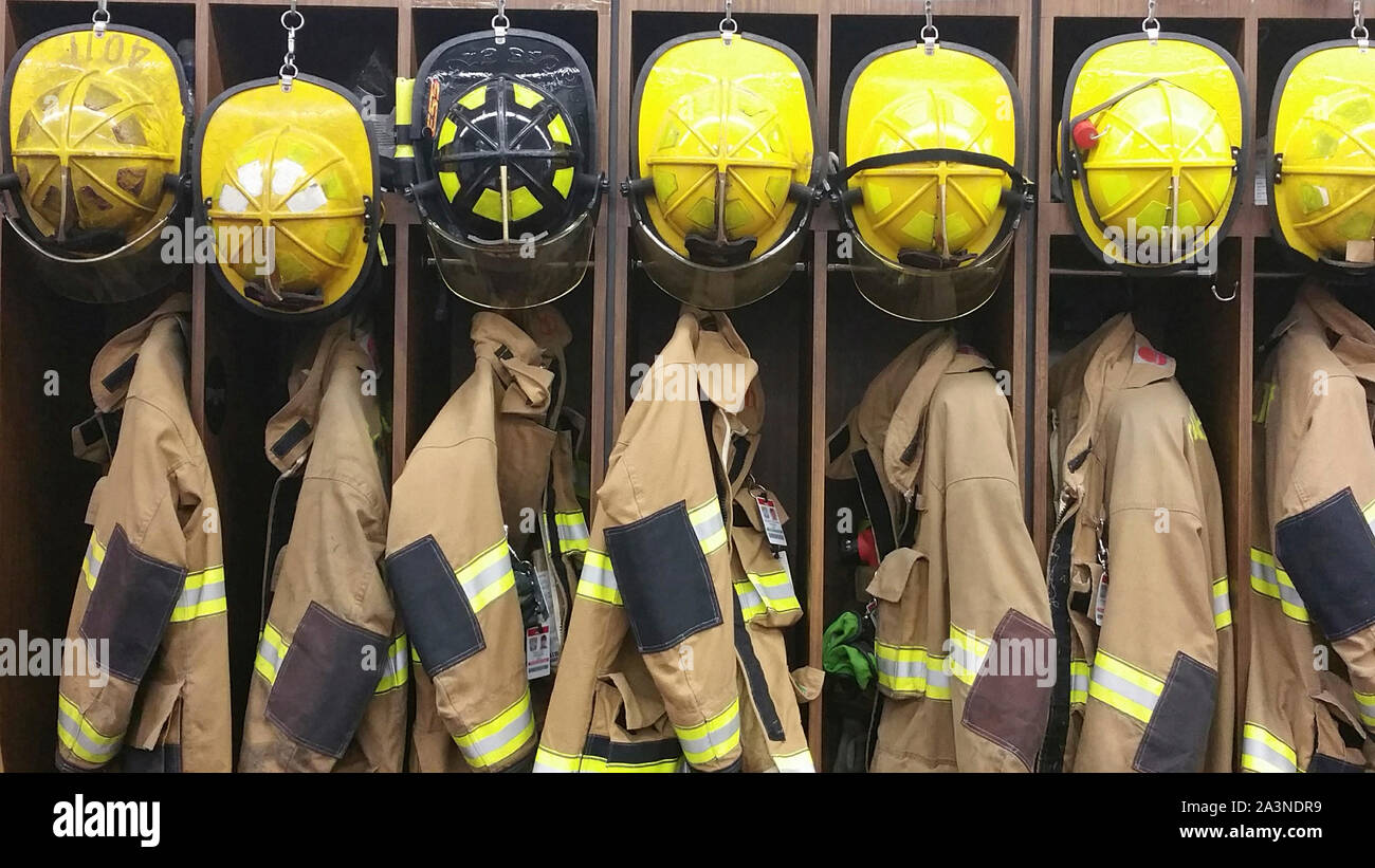 A lineup of firemen’s helmets and turnout gear in a  locker at a volunteer fireman’s station Stock Photo