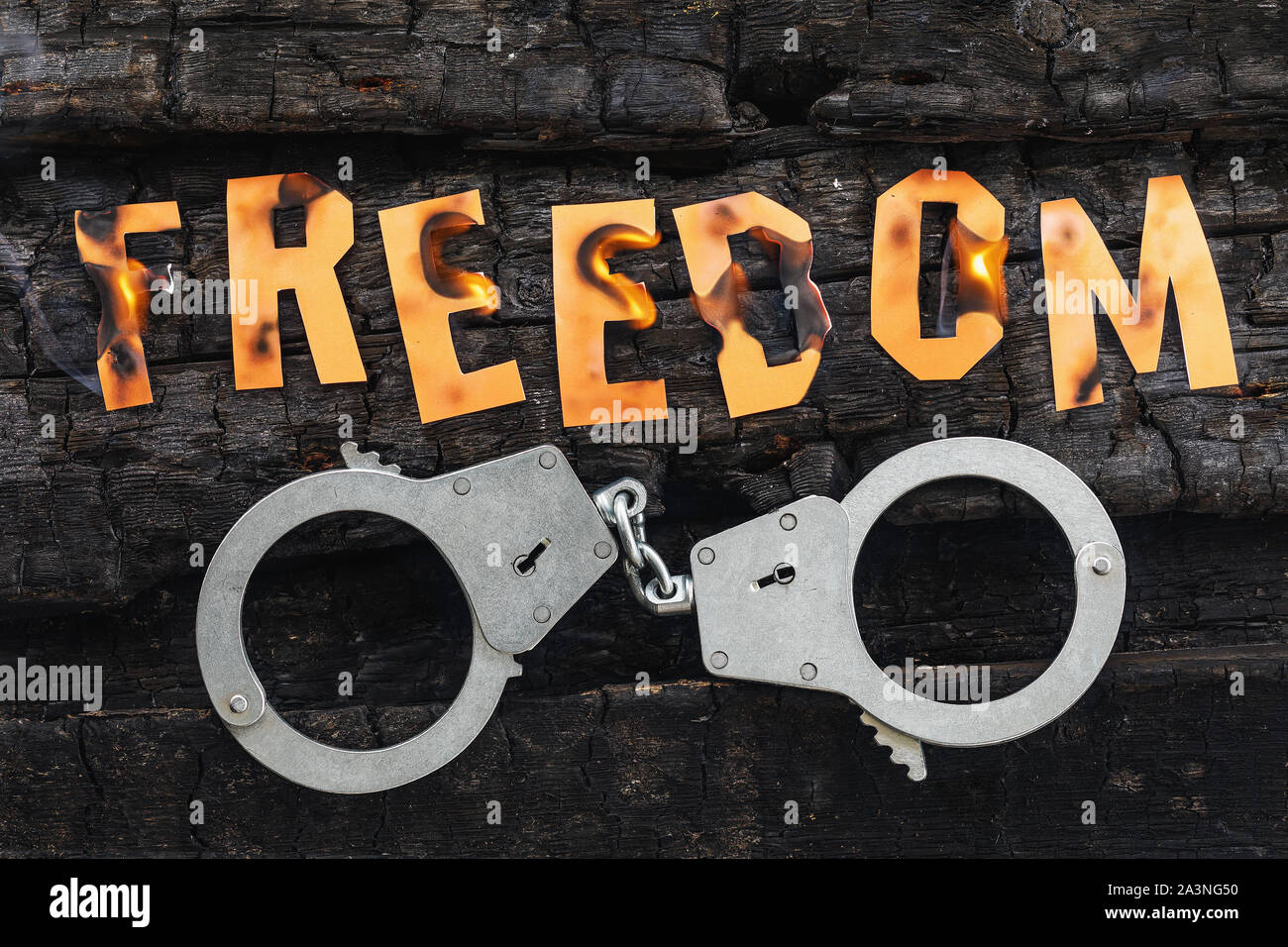 The word freedom burns, and handcuffs lie nearby. Burning letters made of paper. Concept on the topic of hopelessness and lack of trust in justice Stock Photo