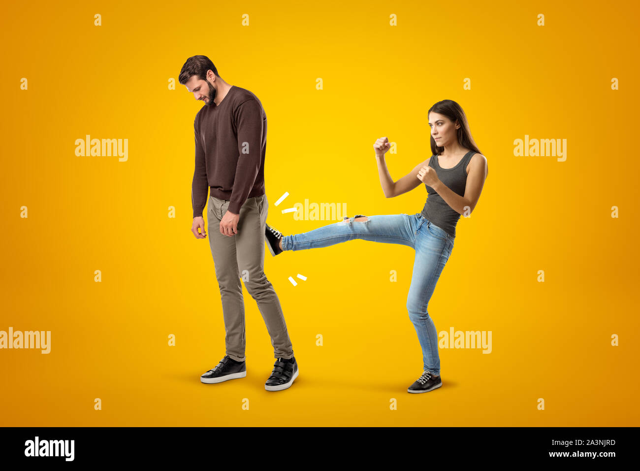 Young brunette girl wearing casual jeans and t-shirt kicking sad young man in casual clothes on yellow background Stock Photo