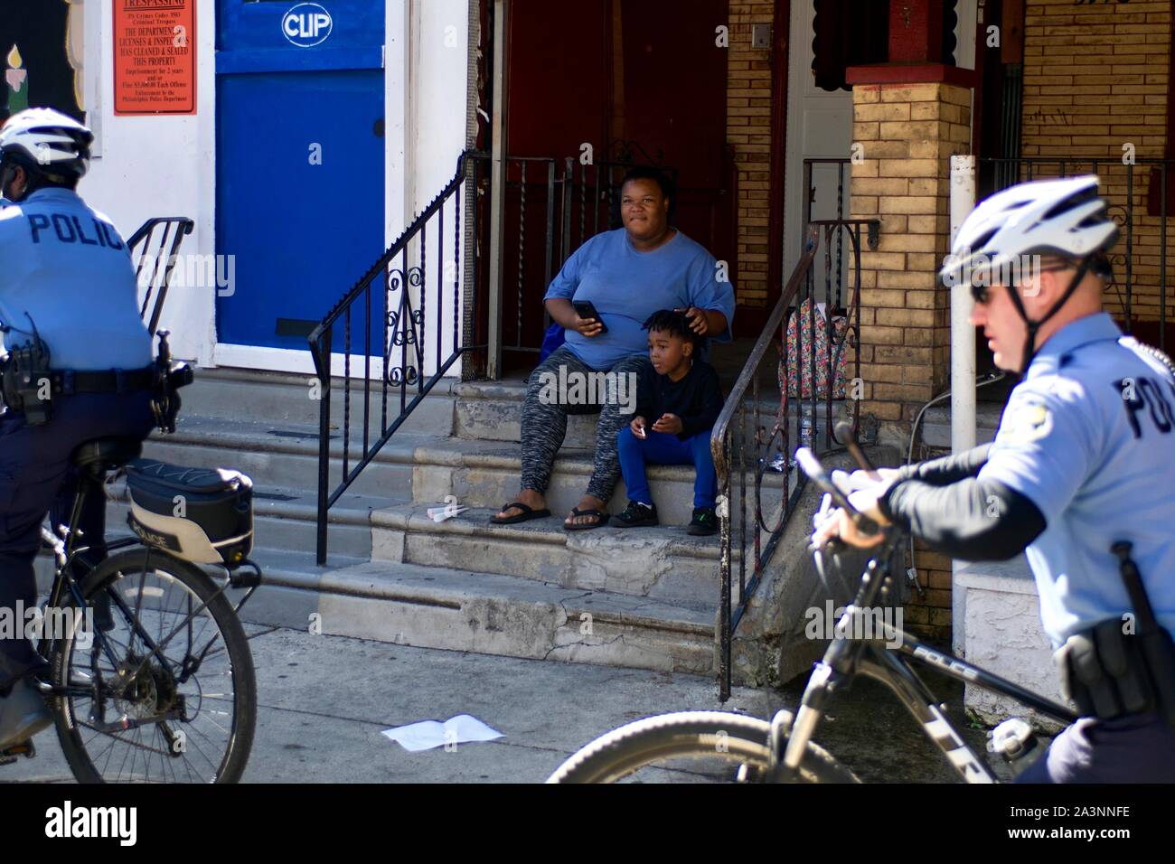Direct neighbor Octavia Abney smiles as she watches from her stoop with son Dylan Abney, 4, when Police officers with a bike patrol unit depart after Stock Photo