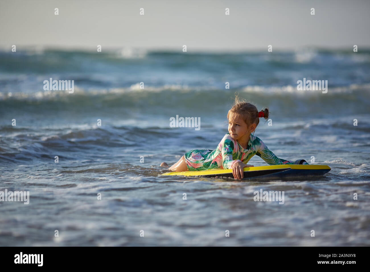 Little baby girl young surfer with bodyboard has a fun on small ocean waves. Active family lifestyle Stock Photo