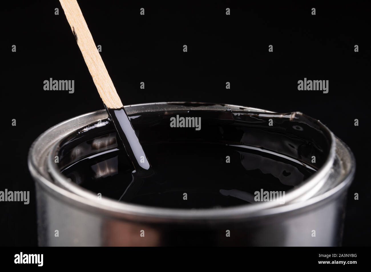 Mixing paint with a wooden stick in a metal can. Preparation of a black emulsion for painting