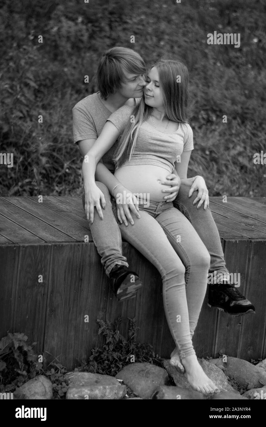 A happy married couple Husband hugs a beautiful adult pregnant wife. walks in a park. Second trimester. Holds his hands on her stomach. The benefits o Stock Photo