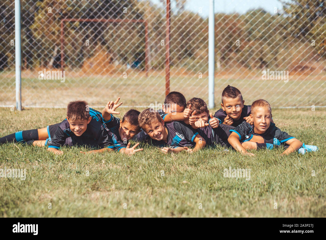Kids soccer football - young children players celebrating victory together while lying on grass. Stock Photo