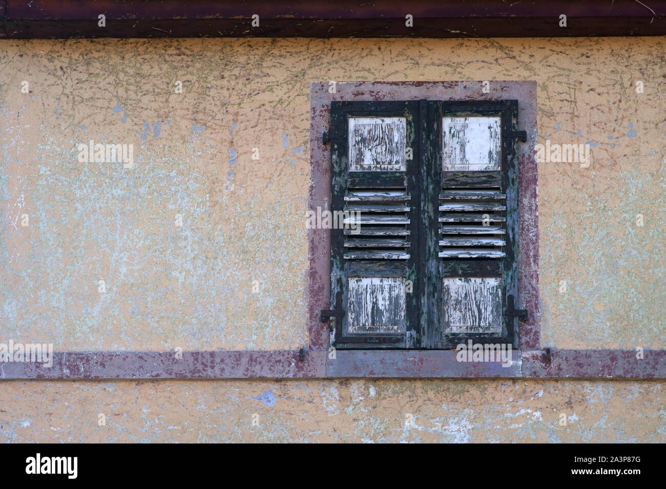 A rotten and dilapidated shutter of a window on a bleached facade. Stock Photo