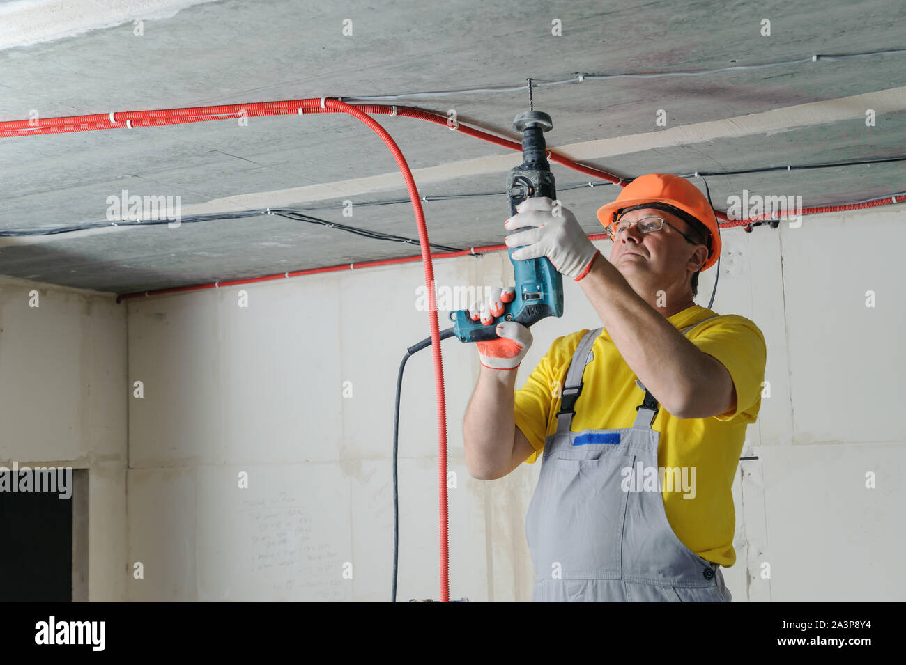 An electrician is drilling a ceiling with a perforator in order to fix the corrugated pipe. Stock Photo