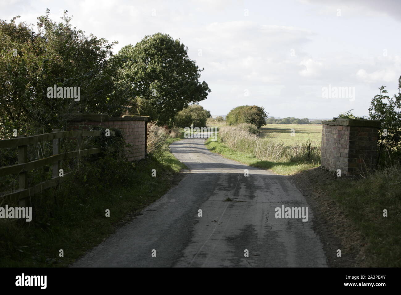 Narrow Rural Country Road with Wooden Stock Fencing and Old Brick Bridge Stock Photo