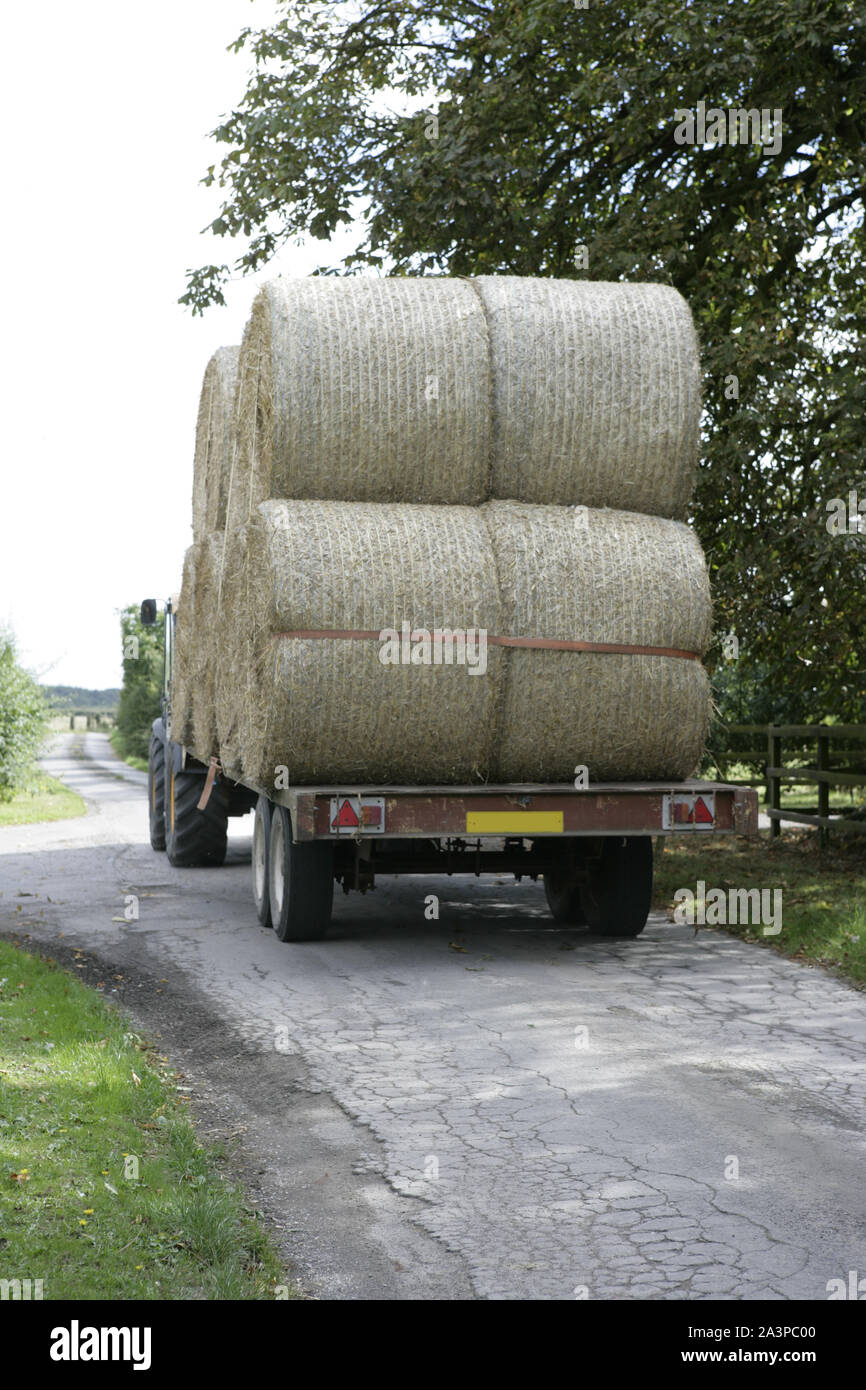 Tractor Trailer Carrying Large Hay Bales on Narrow Country Road Lane Stock Photo