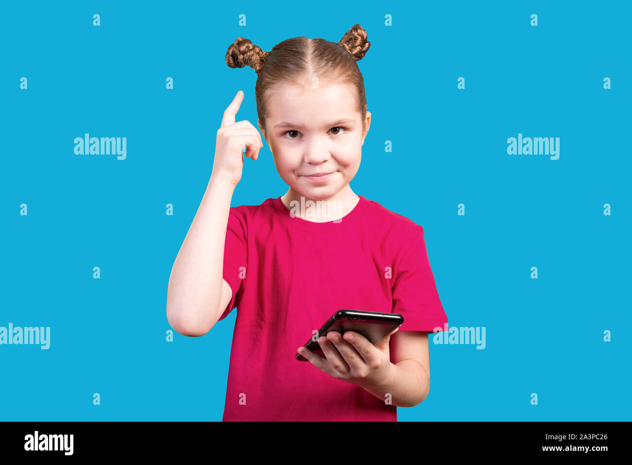Little girl with a pensive facial expression uses a smartphone isolated on a blue background. Stock Photo