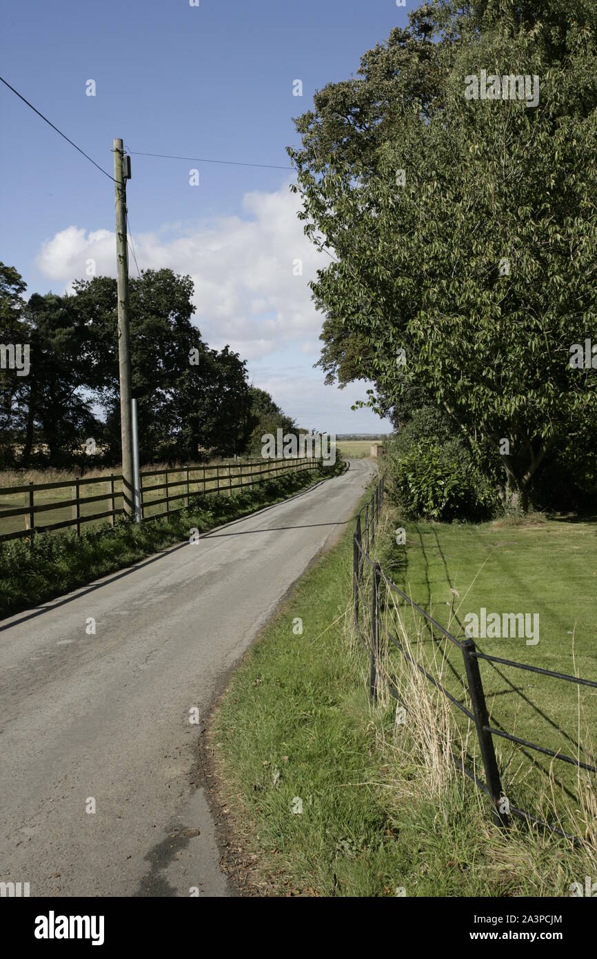 View of Winding Narrow Country Road with Wooden Fencing and Grass Verges Stock Photo