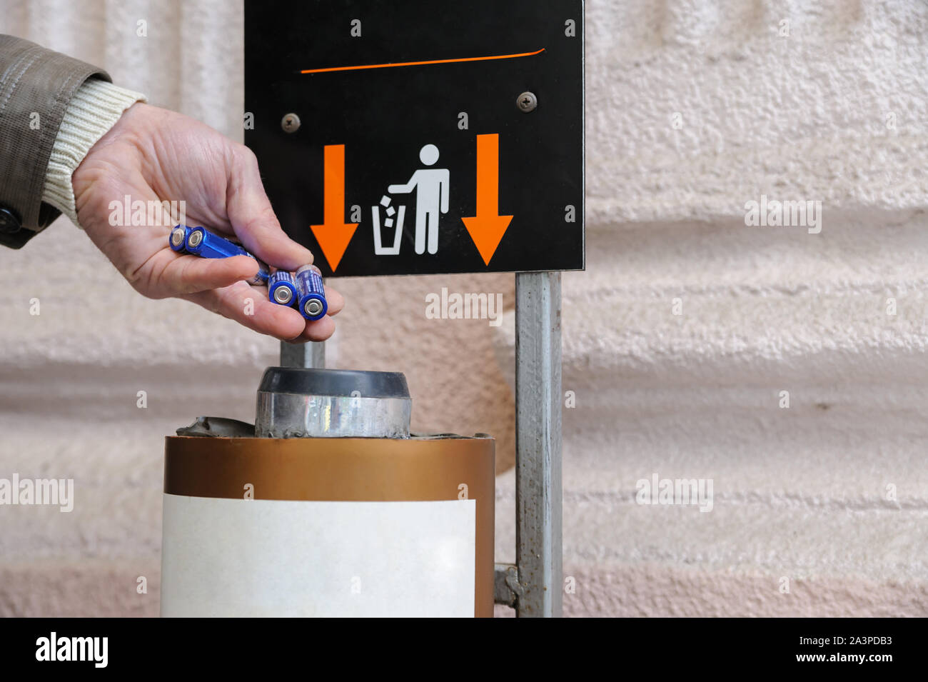 The man's hand is throwing used batteries in a container. Stock Photo