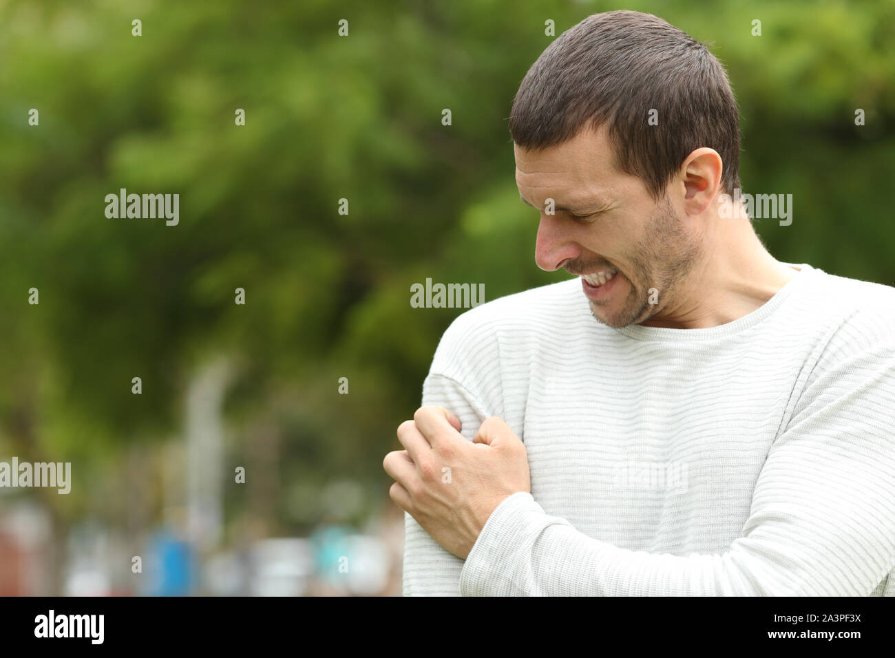 Man suffering itching cratching arm standing in a park Stock Photo