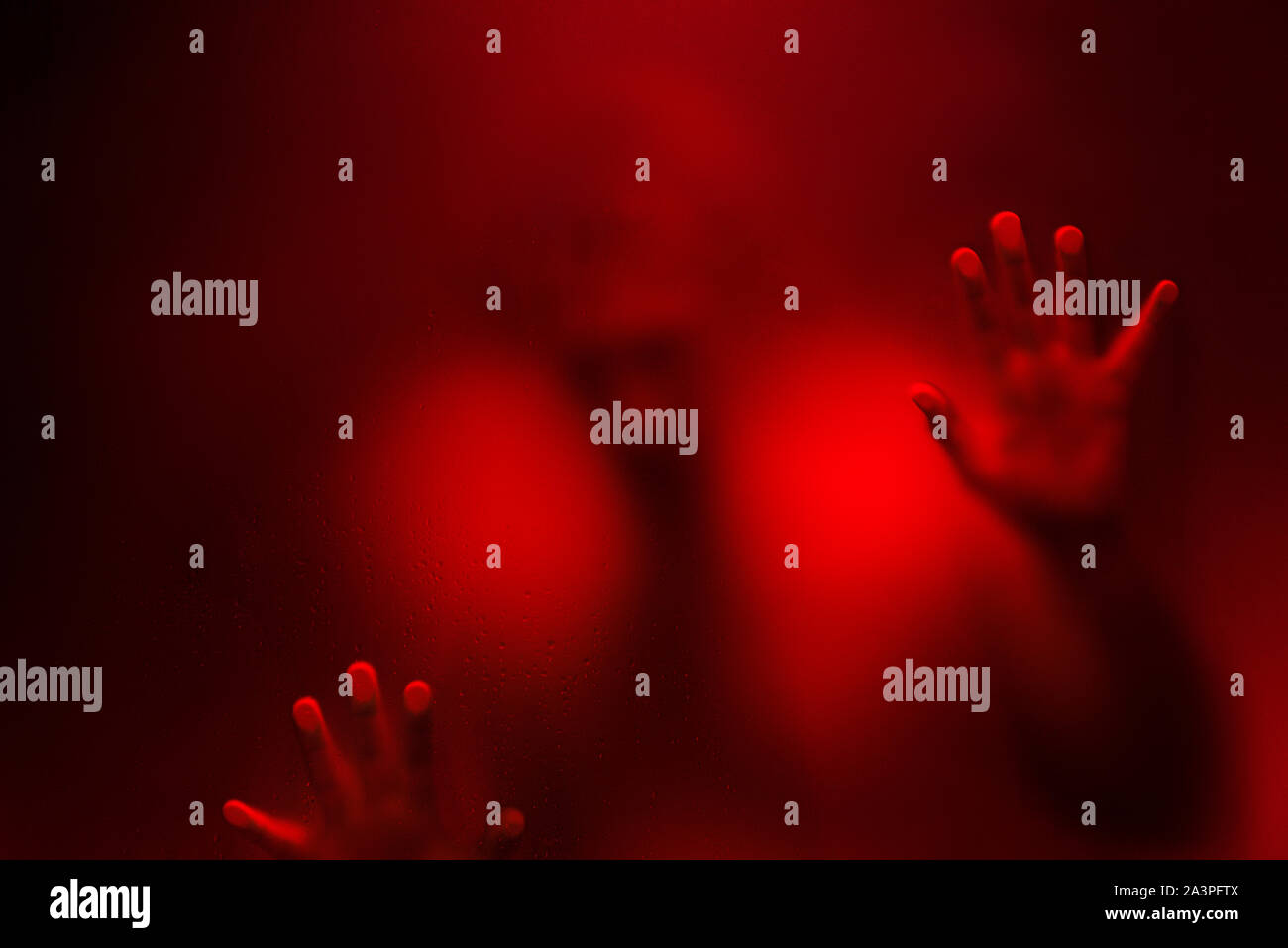 Red color filter version of Creepy man looking behind the frosted glass and  holding it with two hands Stock Photo - Alamy